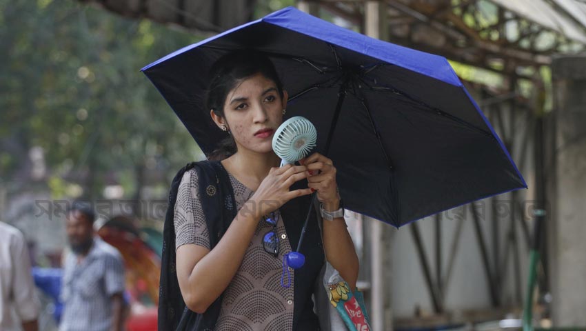 সূর্যের প্রখরতা থেকে রক্ষা পেতে মাথায় ছাতা, হাতে ইলেকট্রিক চার্জার ফ্যান নিয়ে হাঁটছে এক তরুণী। ছবি: সময়ের আলো